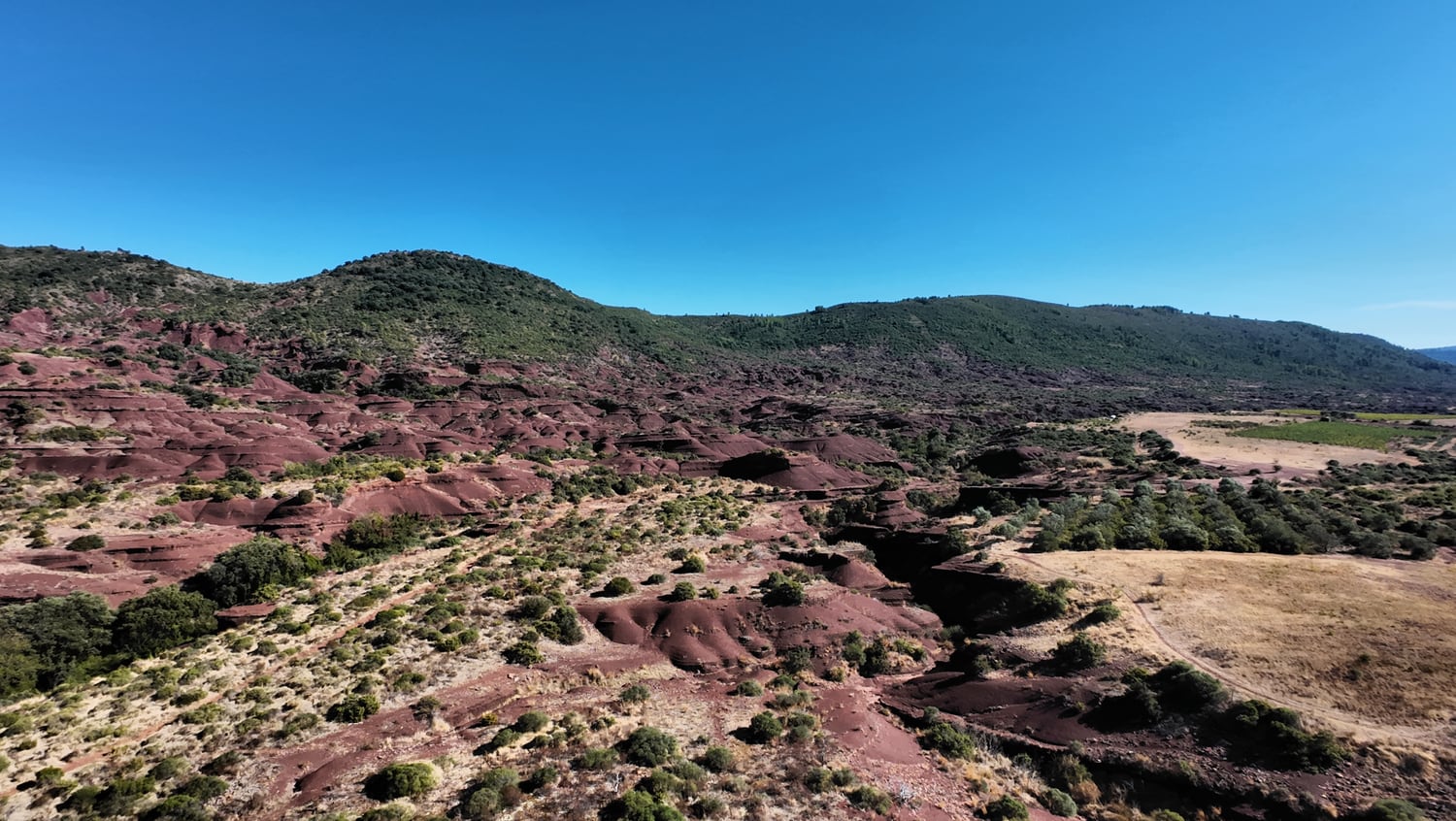 Vue large des ravines rouges du Canyon du Diable, bordées de collines et de parcelles claires sur la droite.