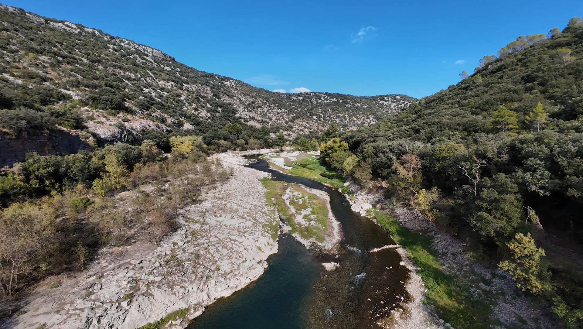 Bande rocheuse claire longeant le cours de l'Hérault, avec des arbres sur les deux rives et les reliefs au loin.