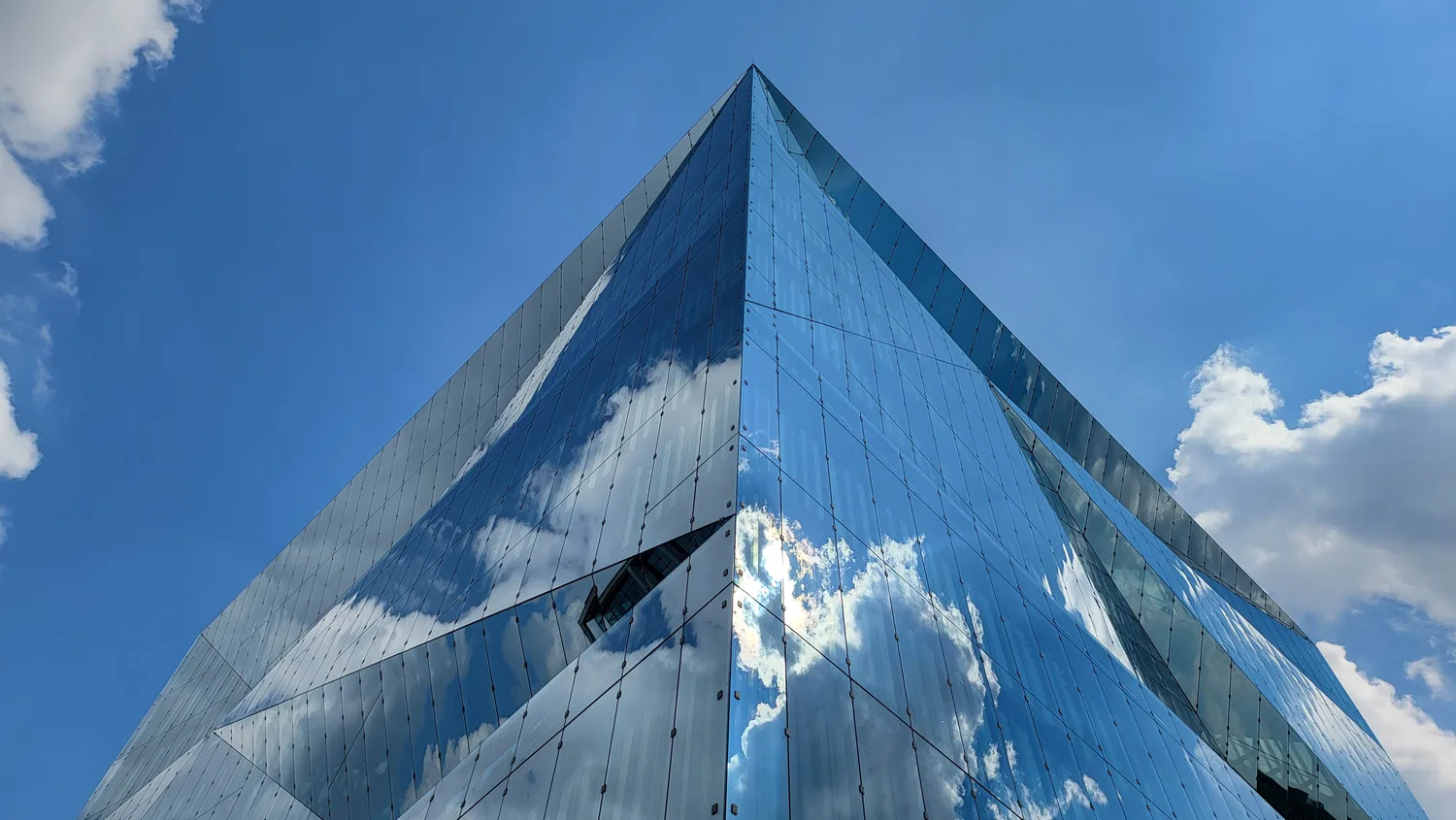 Façade réfléchissante du Cube Berlin photographiée en contre-plongée au smartphone sous un ciel bleu.